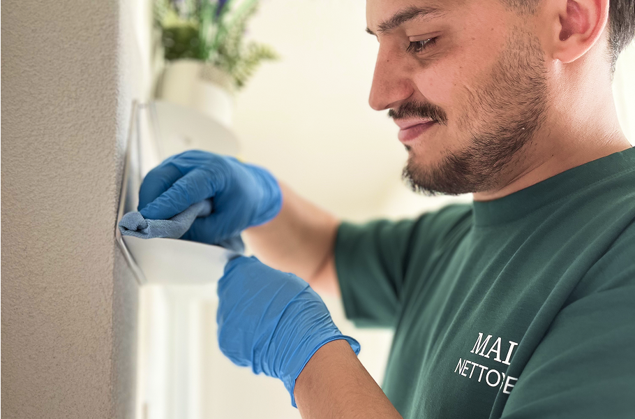 Homme souriant portant un t-shirt Malo Nettoyage nettoyant une surface avec un chiffon microfibre